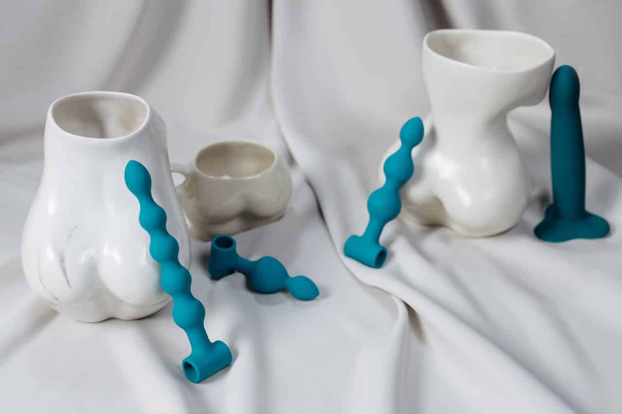 Stylish ceramic vases and turquoise adult toys on a white textile backdrop, evoking sensuality and modern art.